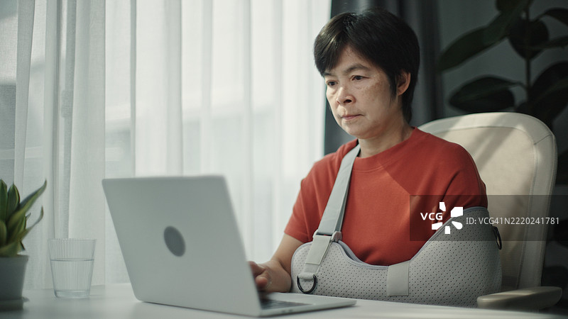 受伤的成熟的女性正在使用笔记本电脑。图片素材