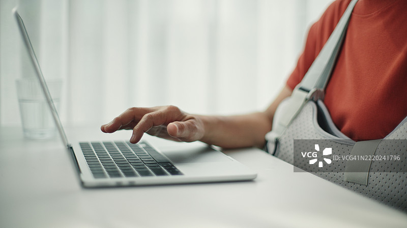 受伤的成熟的女性在使用笔记本电脑。图片素材