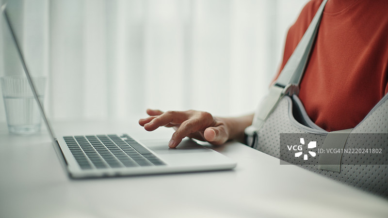 受伤的成熟的女性在使用笔记本电脑。图片素材