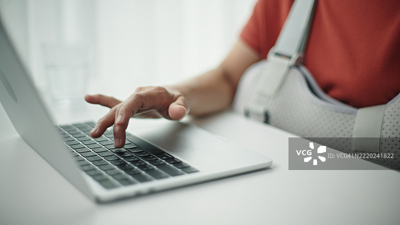 受伤的成熟的女性正在使用笔记本电脑。图片素材