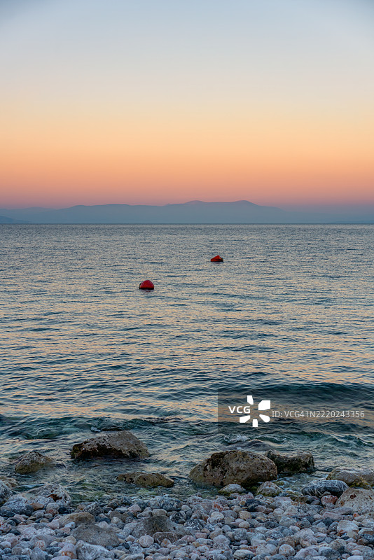 克里奥内里，普雷韦扎，希腊的日落时分，野生卵石海滩，碧绿色的海水和背景中的山脉。图片素材