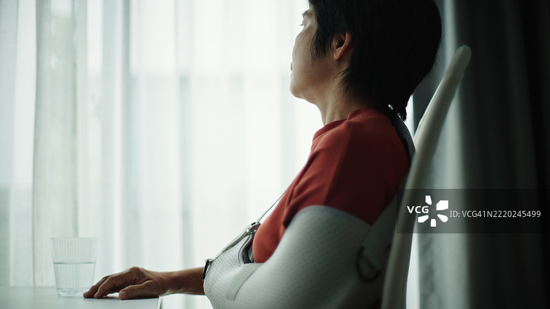 一位手臂打着石膏的成熟的女性望向窗外。图片素材