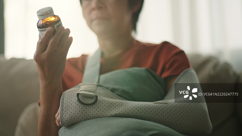 成熟的女性在戴着手臂石膏的情况下阅读维生素补充剂标签。图片素材