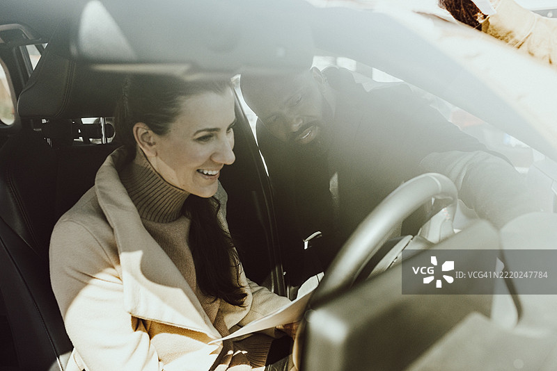 兴奋的女性坐在新车里，销售员通过挡风玻璃解释功能。图片素材