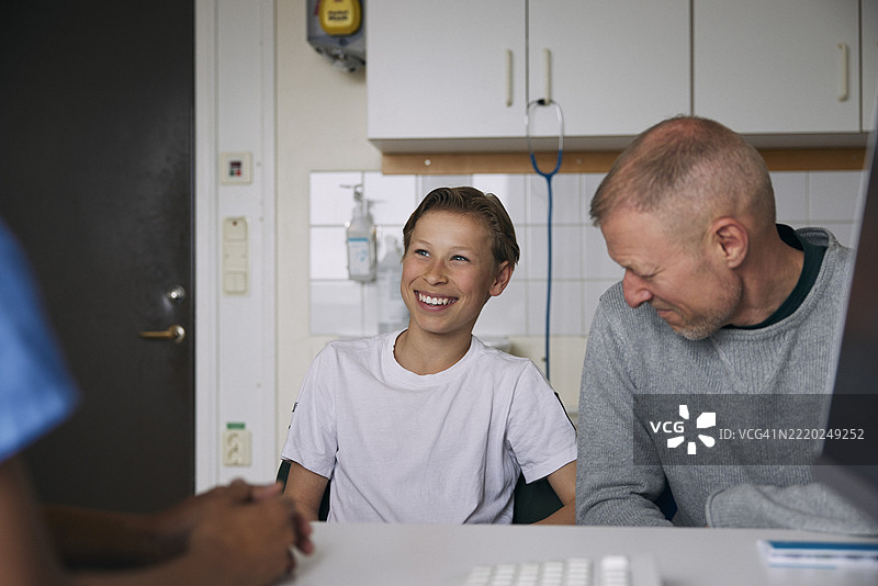 快乐的男孩坐在父亲旁边，与诊所的医生讨论图片素材