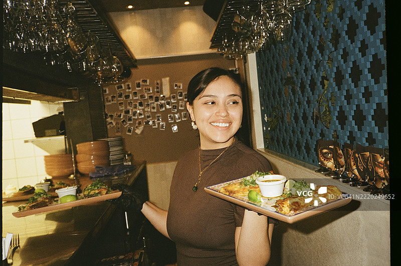 微笑的年轻女性在厨房里端着快餐托盘图片素材