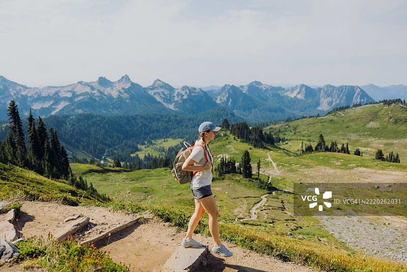 愉快的女性背着背包在雷尼尔山徒步旅行，欣赏夏季户外美景图片素材