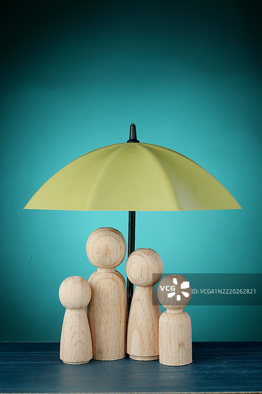 用绿色雨伞保护的木制家庭人偶图片素材