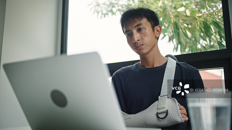 受伤的男子在使用笔记本电脑。图片素材