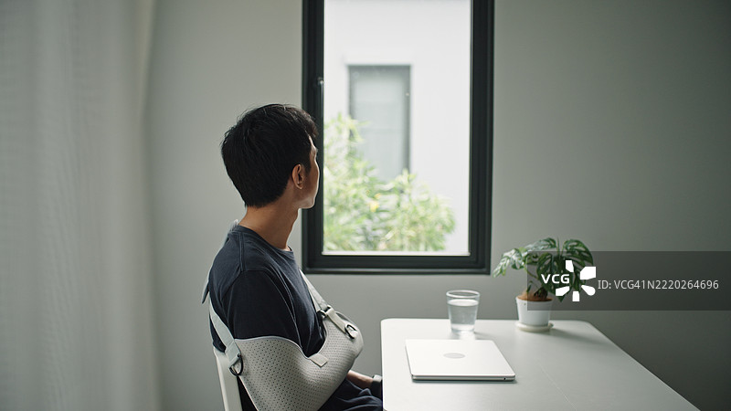 戴着手臂石膏的男子在工作中休息。图片素材