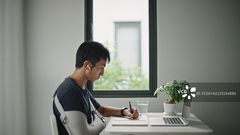 戴着手臂石膏的男子在线学习。图片素材