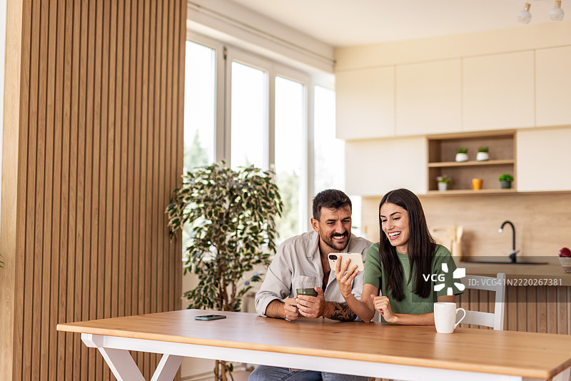 快乐的情侣在家里看手机上的搞笑内容图片素材