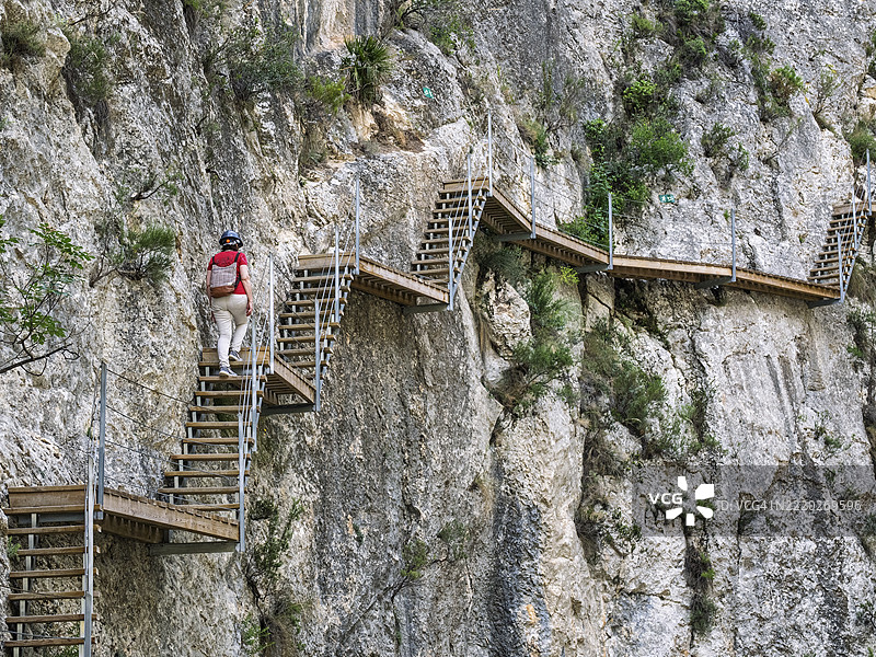 冒险旅游，一位女性正在攀爬嵌入峡谷岩壁的木栈道。雷尤桥（Pasarela de Relleu）图片素材