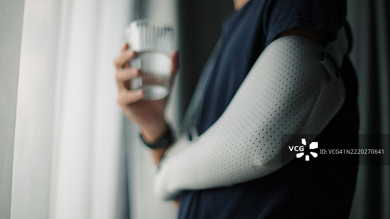 戴着手臂石膏的男子在喝水。图片素材