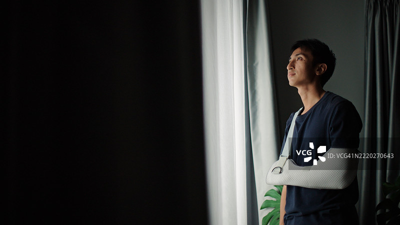 戴着手臂石膏的男子望向窗外。图片素材