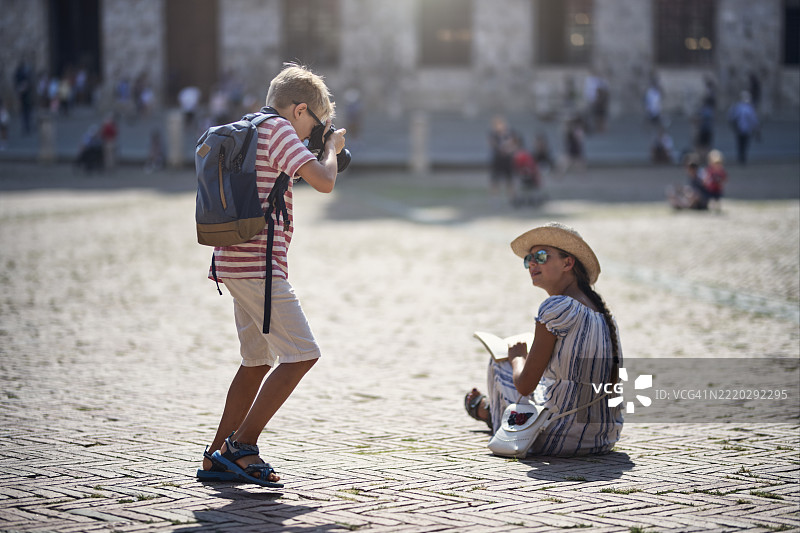 小男孩在坎波广场给正在读书的姐姐拍照。图片素材