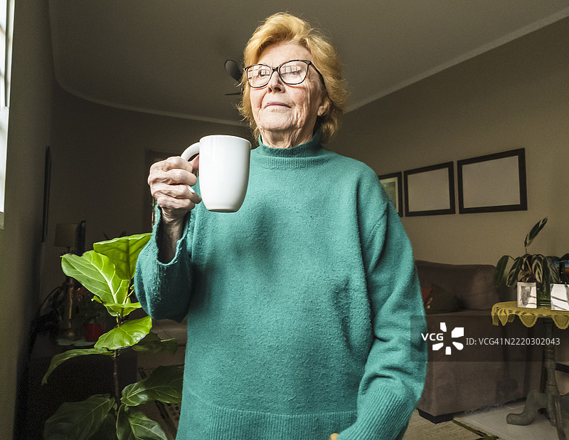 温馨客厅中拿着咖啡杯的老年女性图片素材