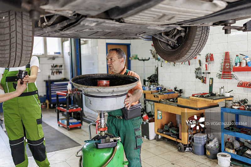男性和女性机械师使用液体抽取器进行换油作业图片素材