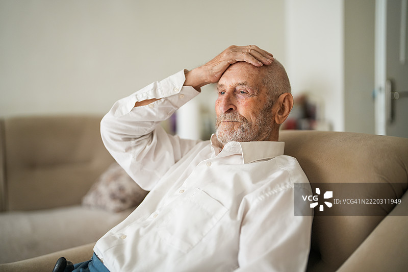 孤独的老年男子在家中沉思，手持拐杖。图片素材