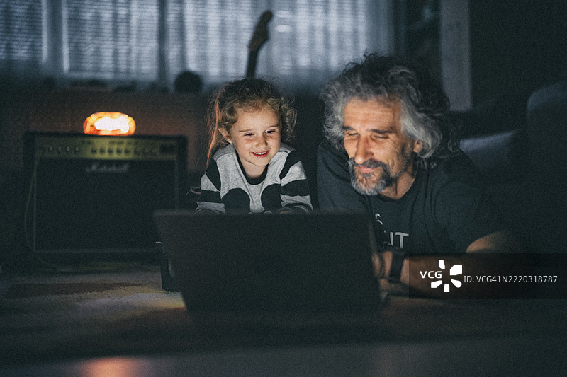 全家人在深夜一起享受乐趣。爸爸和孩子在笔记本电脑上看电视。图片素材
