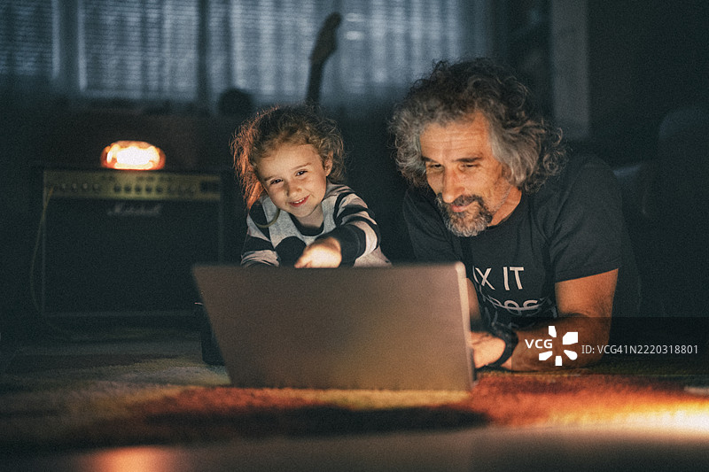 家庭乐趣深夜时光。爸爸和孩子在温馨的灯光下用笔记本电脑看电视。图片素材