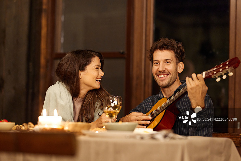快乐的男人在露台上为妻子弹吉他，享受美好的一餐。图片素材