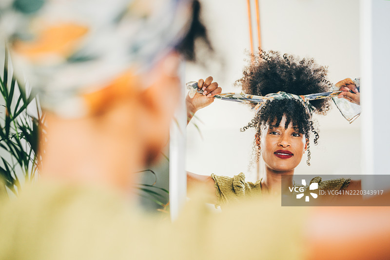 一位女性在镜子前整理她的卷发。图片素材