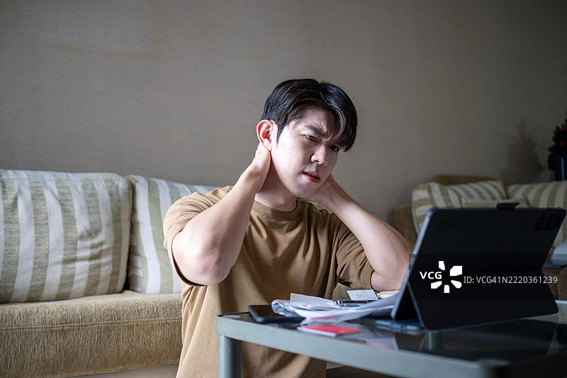 亚洲青少年男子在客厅用笔记本电脑熬夜工作感到压力图片素材