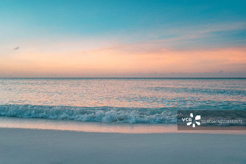 宁静的日落海滩特写，温柔的海浪、柔软的沙滩和热带岛屿上闪耀的夏日天空，完美的美丽风景，适合度假、自然和放松灵感的背景。图片素材