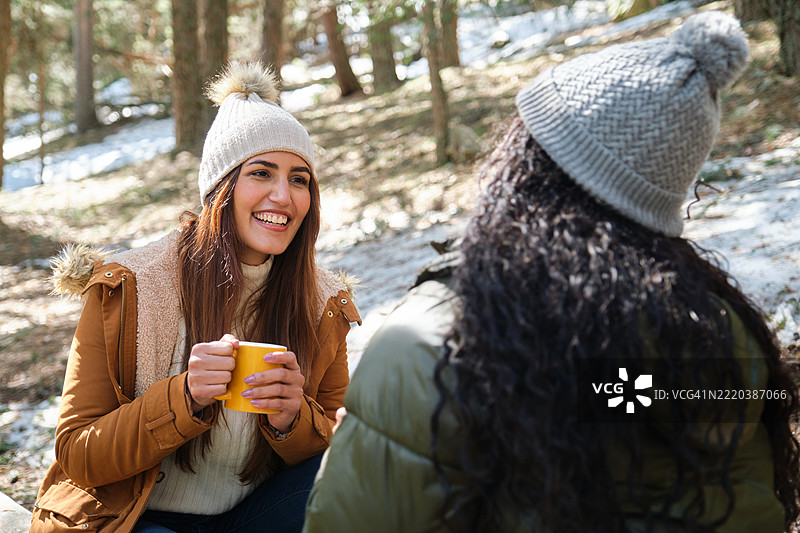 两个快乐的女性朋友在雪-covered森林中享受热饮图片素材