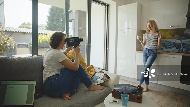 两位白人女性在明亮的自然光下，悠闲地在家中使用复古相机。图片素材