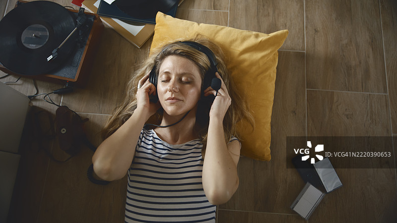 年轻女性在室内放松，佩戴复古耳机，旁边有一台唱片播放器。图片素材