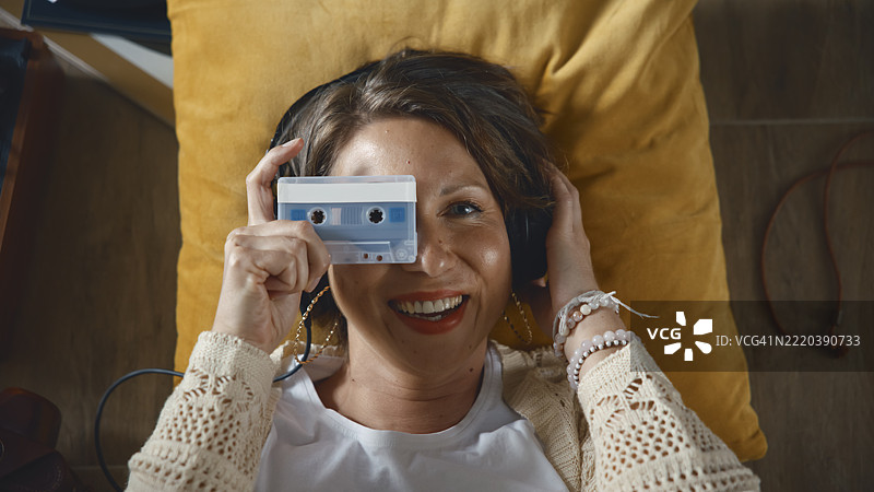 微笑的女性佩戴复古耳机，手中拿着一盘卡带图片素材