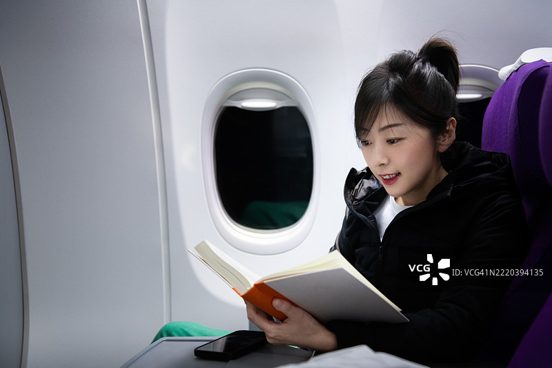 女性在飞机窗边阅读书籍图片素材