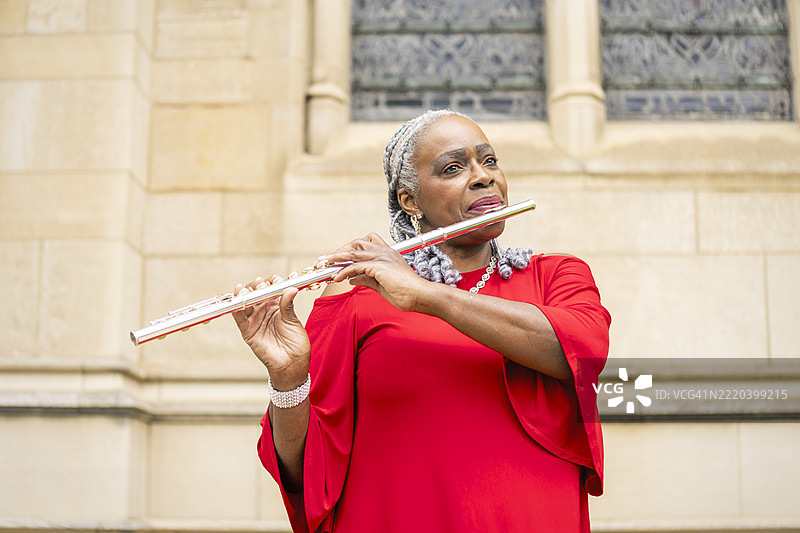 穿着红色裙子的美丽女性在户外吹奏长笛图片素材