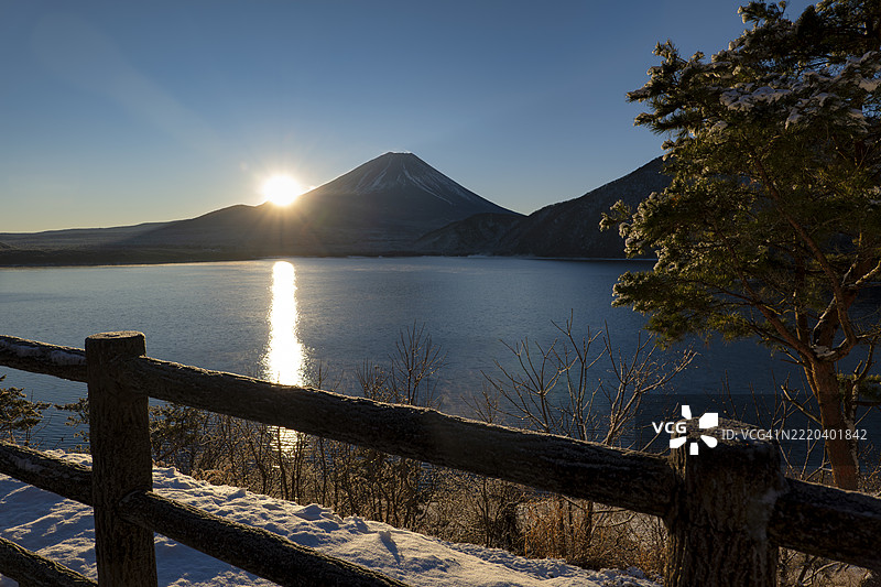 富士山在早晨日出时映照在本栖湖上，前景是被雪覆盖的湖岸（概念；初日，元旦的第一缕阳光，新年）图片素材