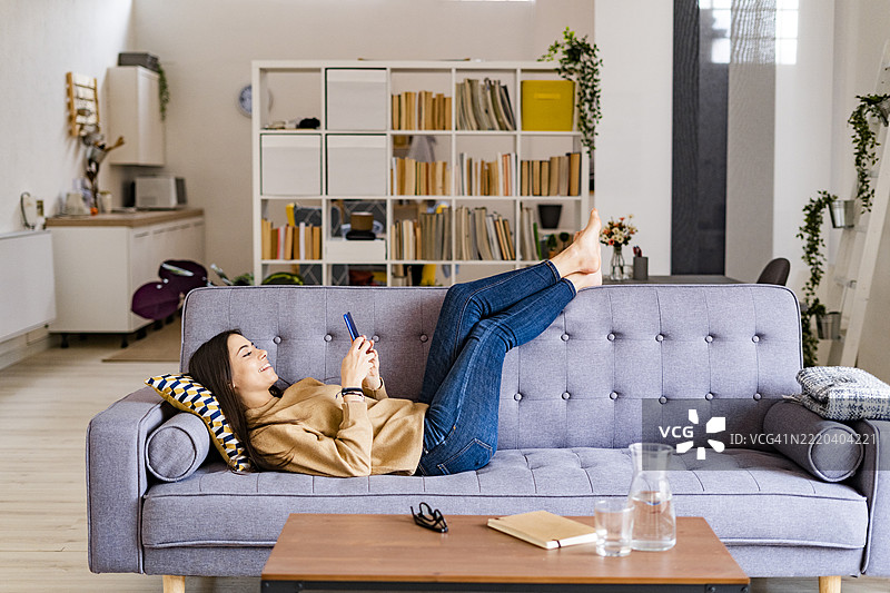年轻女性在家放松时使用智能手机图片素材