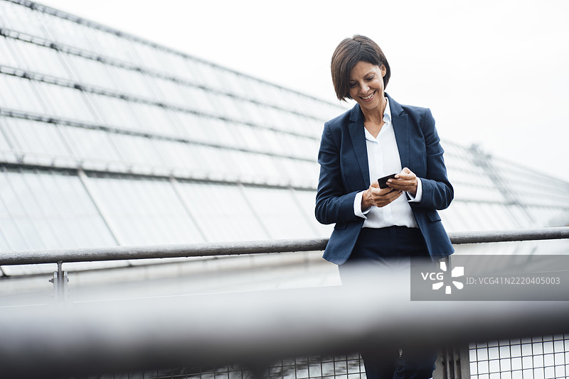 微笑的女商人在办公楼外用手机发短信图片素材