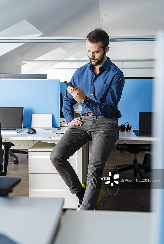 年轻商人在办公室桌子上坐着使用手机图片素材