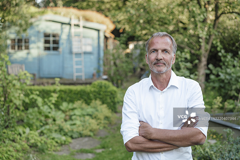 双臂交叉站在花园里的严肃男人图片素材