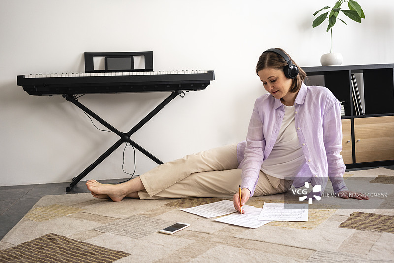 中年女性在家中戴着耳机写纸上的内容图片素材