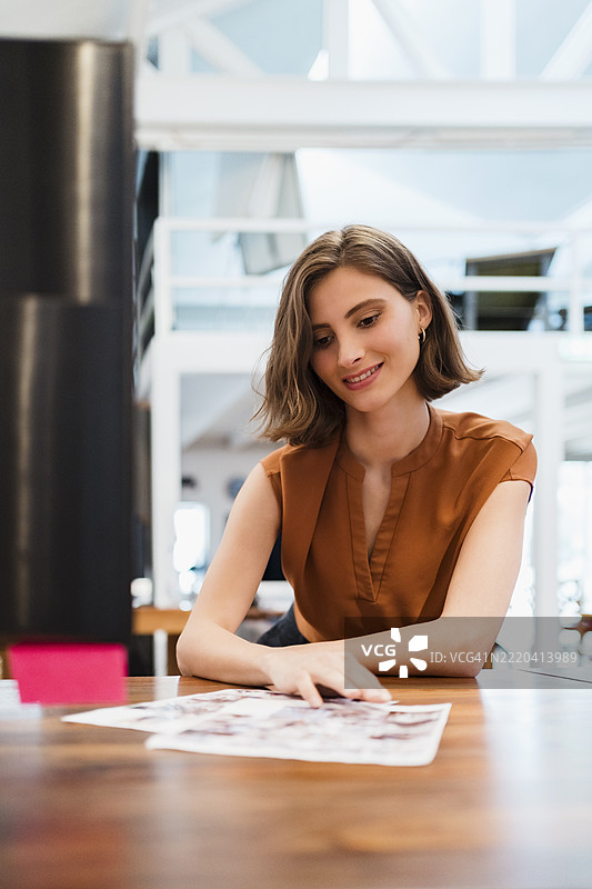 微笑的女商人坐在创意办公室的桌子前分析文件图片素材