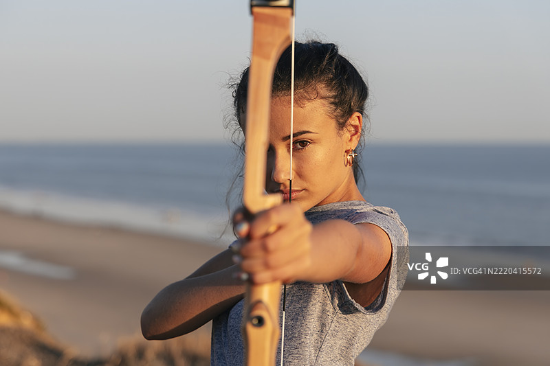 专注的女性在海滩上拉弓射箭图片素材