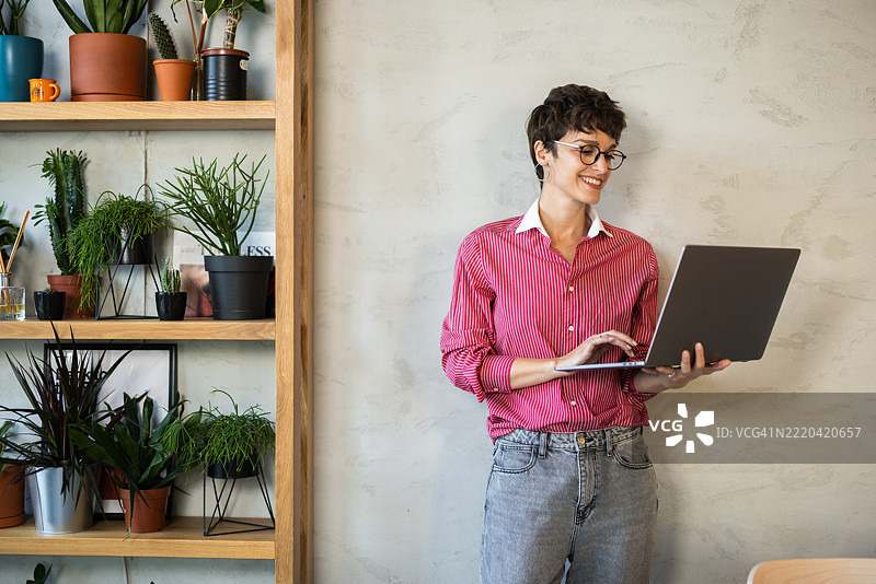 年轻女商人在现代办公室中使用笔记本电脑，周围有植物。图片素材