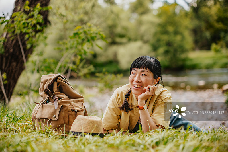 快乐的女人在阳光明媚的日子里享受自然，坐在河边，拥抱户外冒险与放松。图片素材