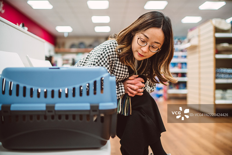 女子在兽医诊所安慰她的猫咪运输箱中的猫。图片素材