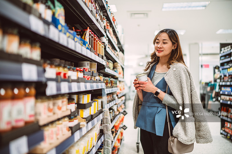 女性在超市过道比较商品，进行日常购物。图片素材