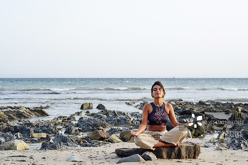 年轻女性在海滩的岩石上练习莲花坐姿图片素材
