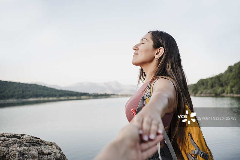 女性徒步旅行者闭着眼睛在湖边握着朋友的手，享受假期。图片素材