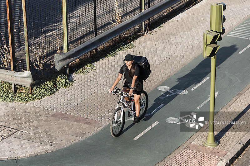 年轻女性前线工作者在阳光明媚的日子里骑自行车停在红绿灯前图片素材